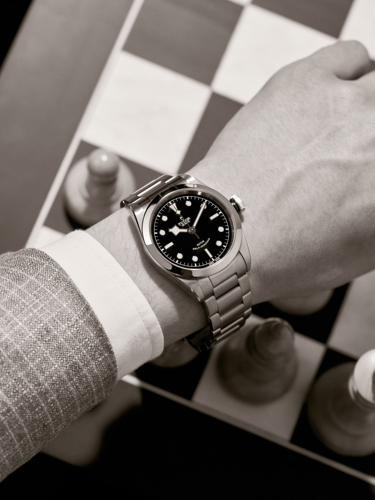 Heritage Black Bay 41 by Tudor watch with black dial on wrist wearing white cuff and gray jacket.