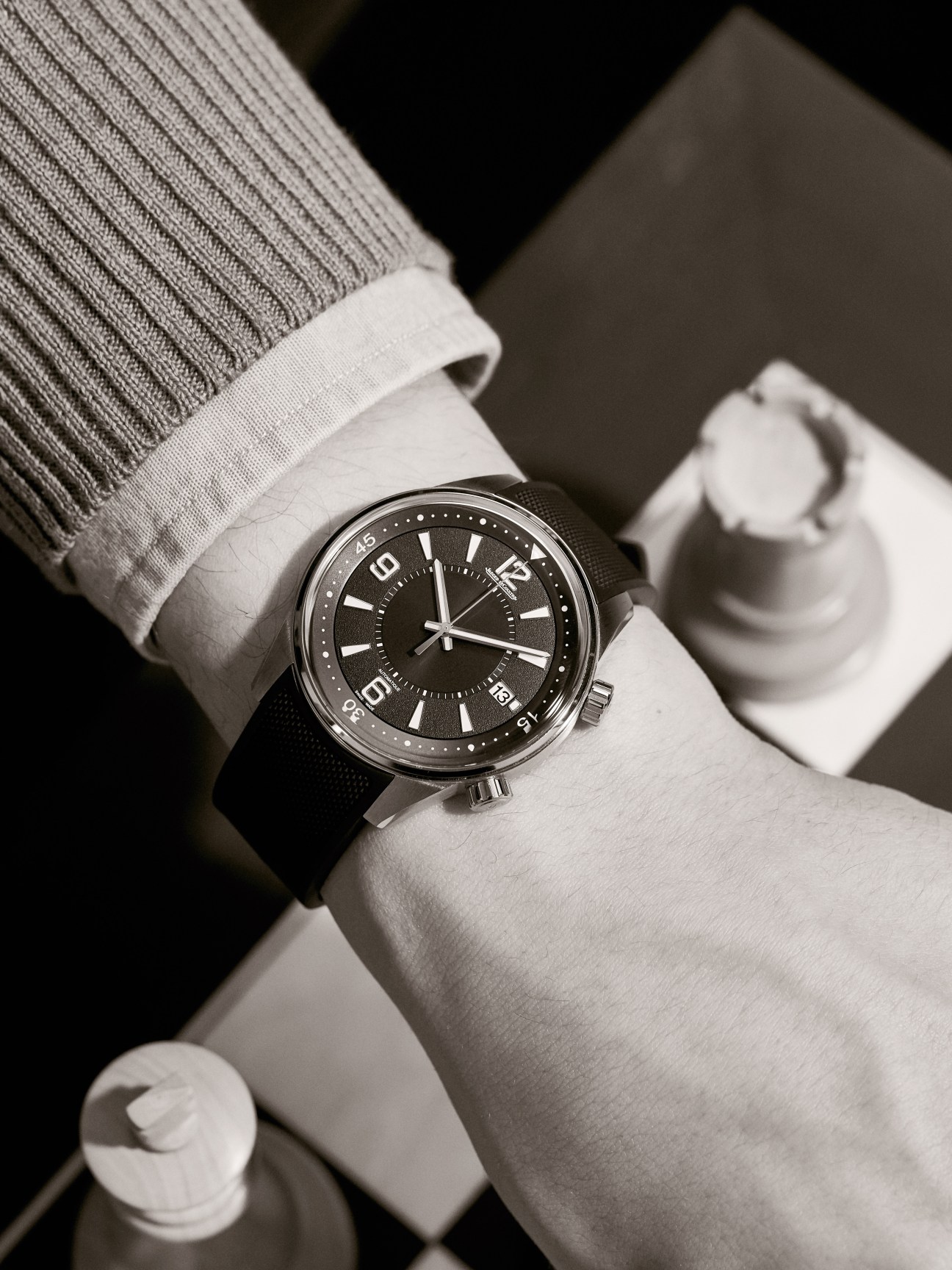 Polaris Date by Jaeger-LeCoultre watch with black dial worn on wrist with white shirt cuff and gray cardigan.