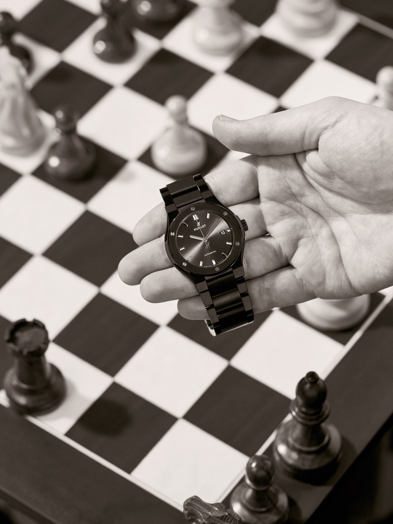 Classic Fusion Ceramic Blue by Hublot watch held in hand above a chessboard.
