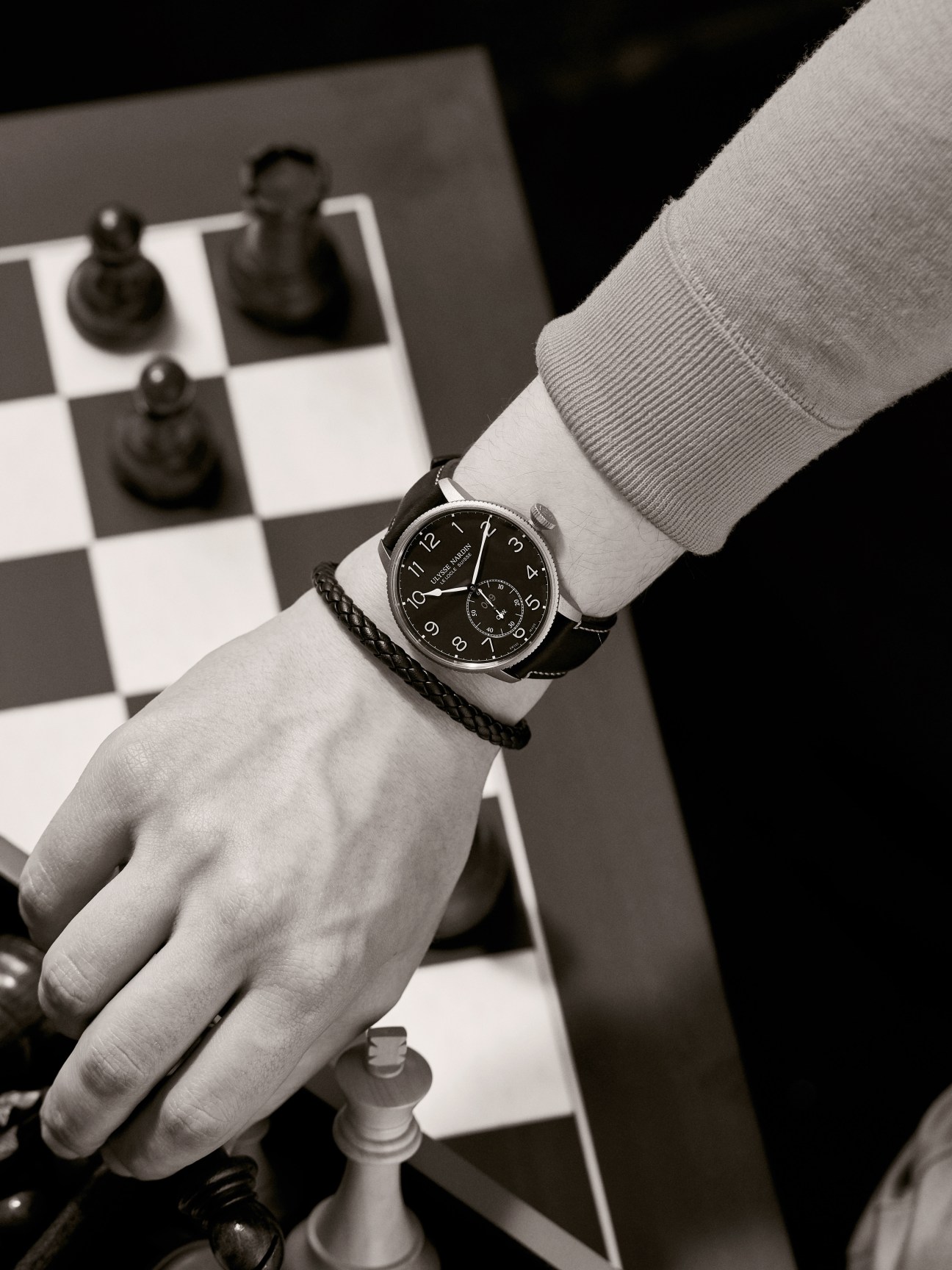 Wrist wearing a black Marine Torpilleur Limited Edition watch by Ulysse Nardin over a chessboard.