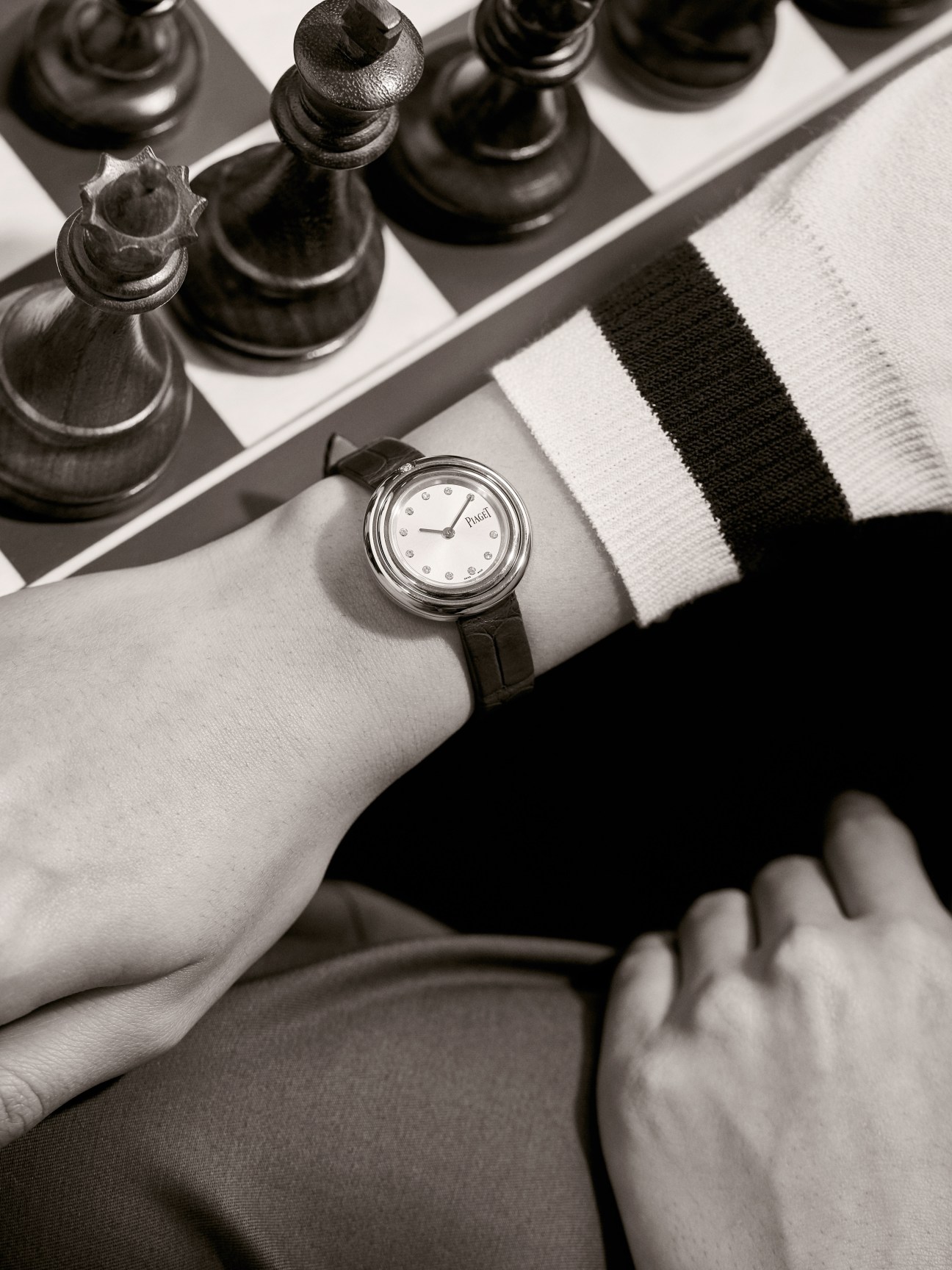 Possession watch by Piaget worn on wrist with striped jumper, styled chess pieces in background.