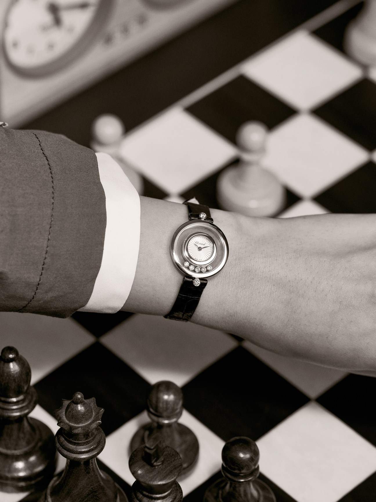 Happy Diamonds by Chopard watch with diamond bezel on woman's wrist above chessboard.