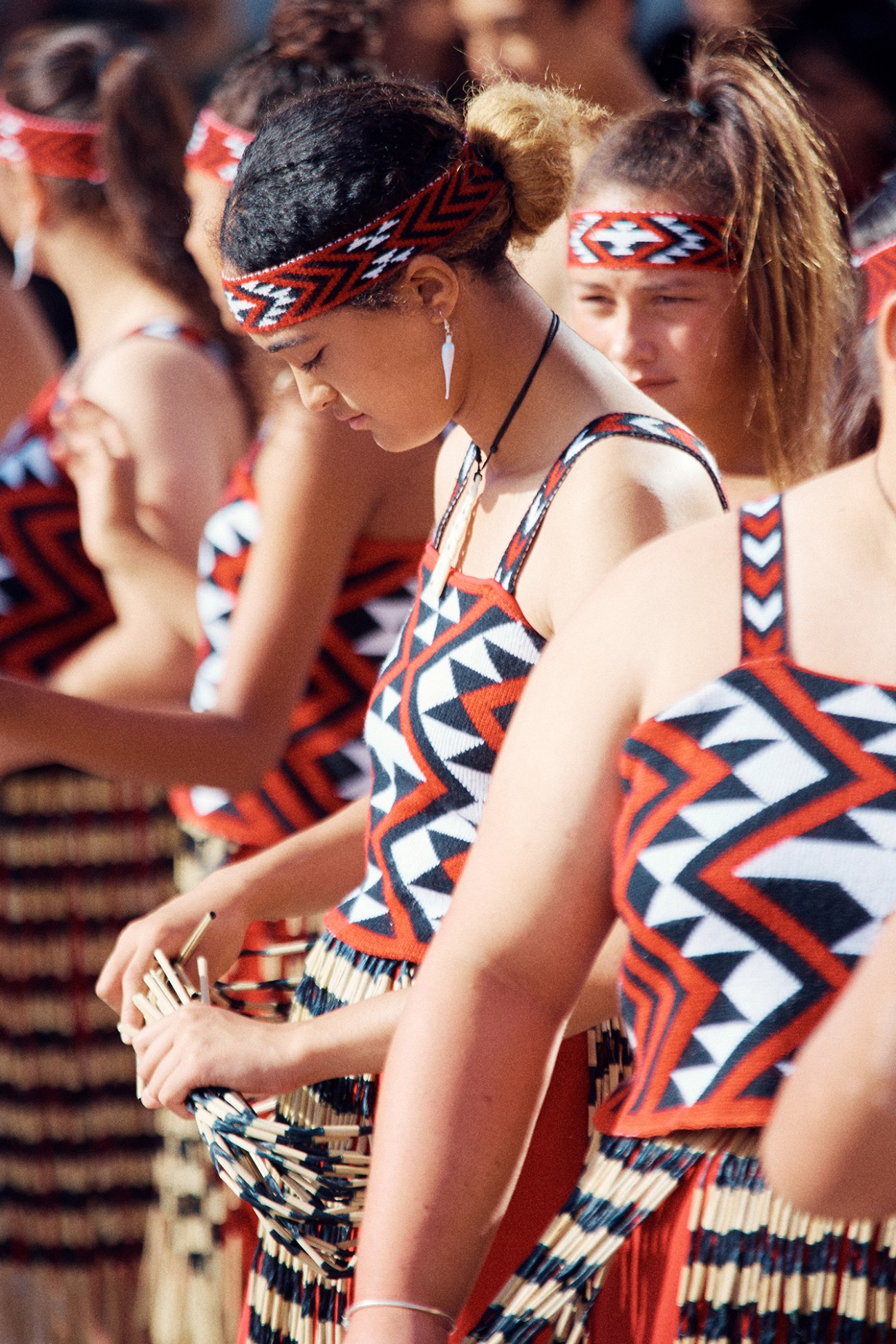 Indigenous Māori women in traditional red and black geometric patterned dress at a cultural performance.