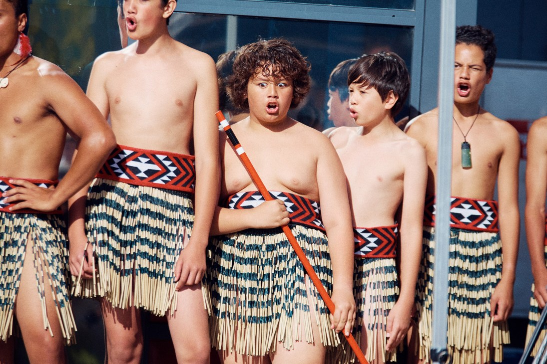 Māori performers in traditional dress performing a haka with weapons.
