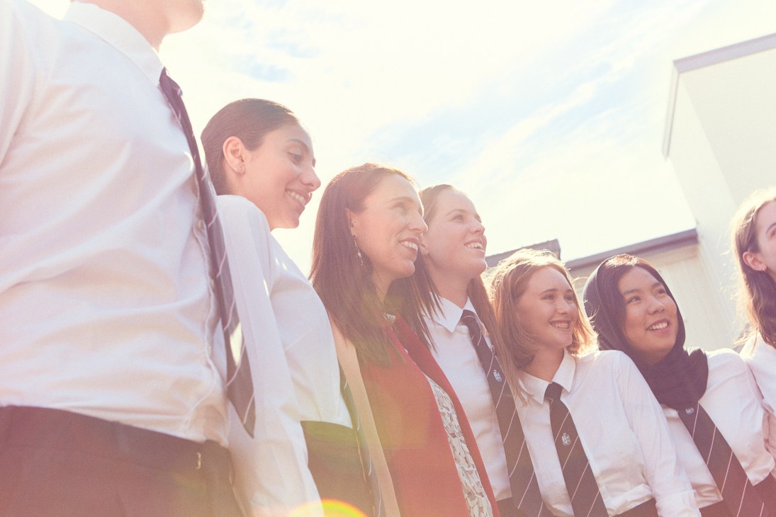 New Zealand Prime Minister Jacinda Ardern smiling while standing with a group of school students in uniforms at Selwyn College, Auckland.