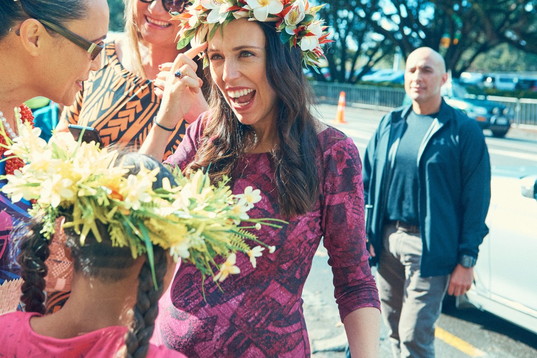 Jacinda Ardern wearing a flower crown and purple top smiles while greeting festival attendees at the Pasifika Festival in Auckland.
