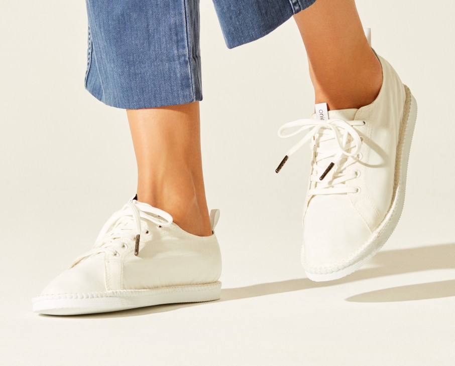 Model wearing blue jeans and white lace-up shoes by Onia against a neutral background.