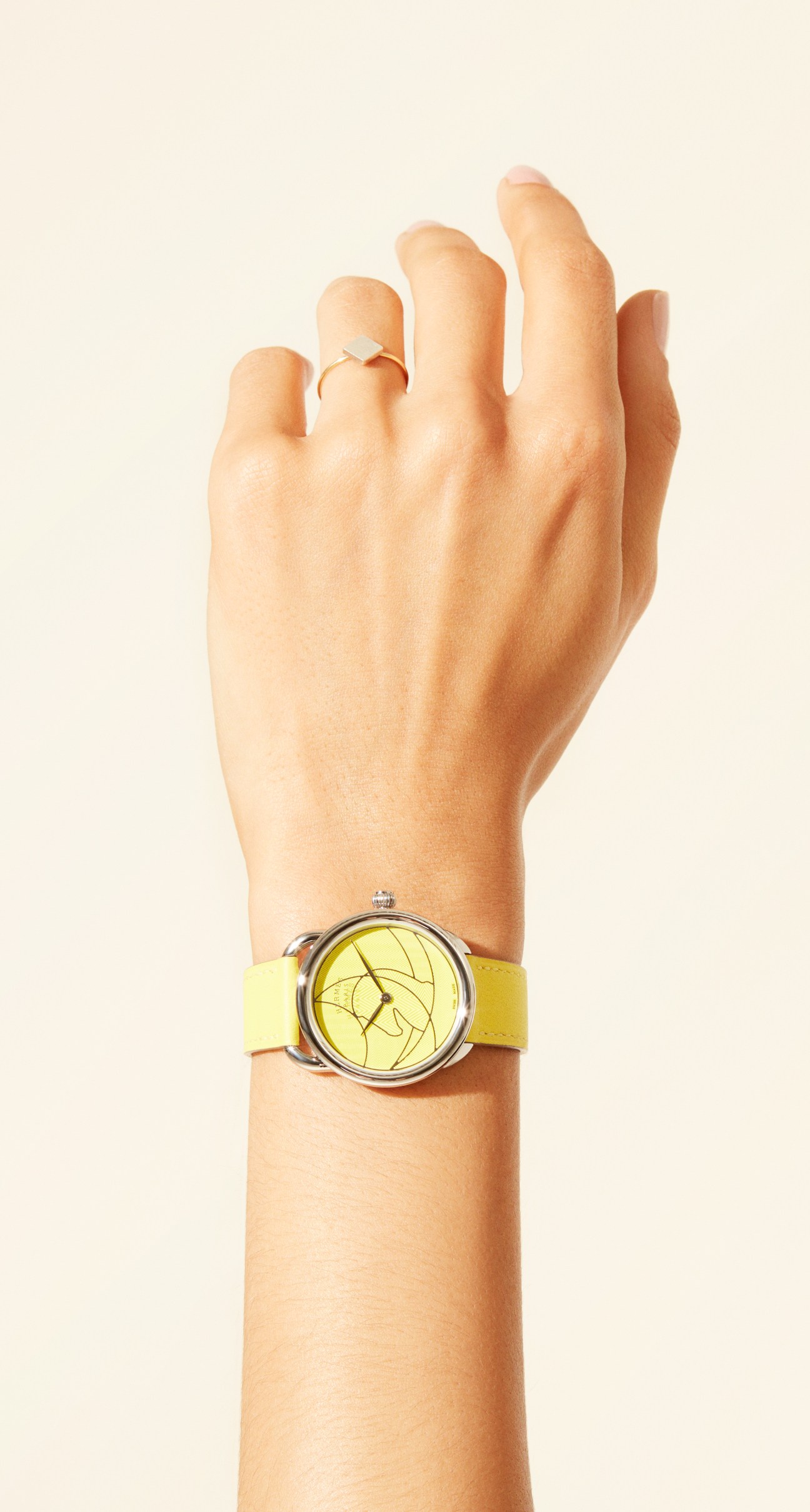 Hand displaying a Hermès watch with yellow leather strap and ring by Stephanie Cachard.