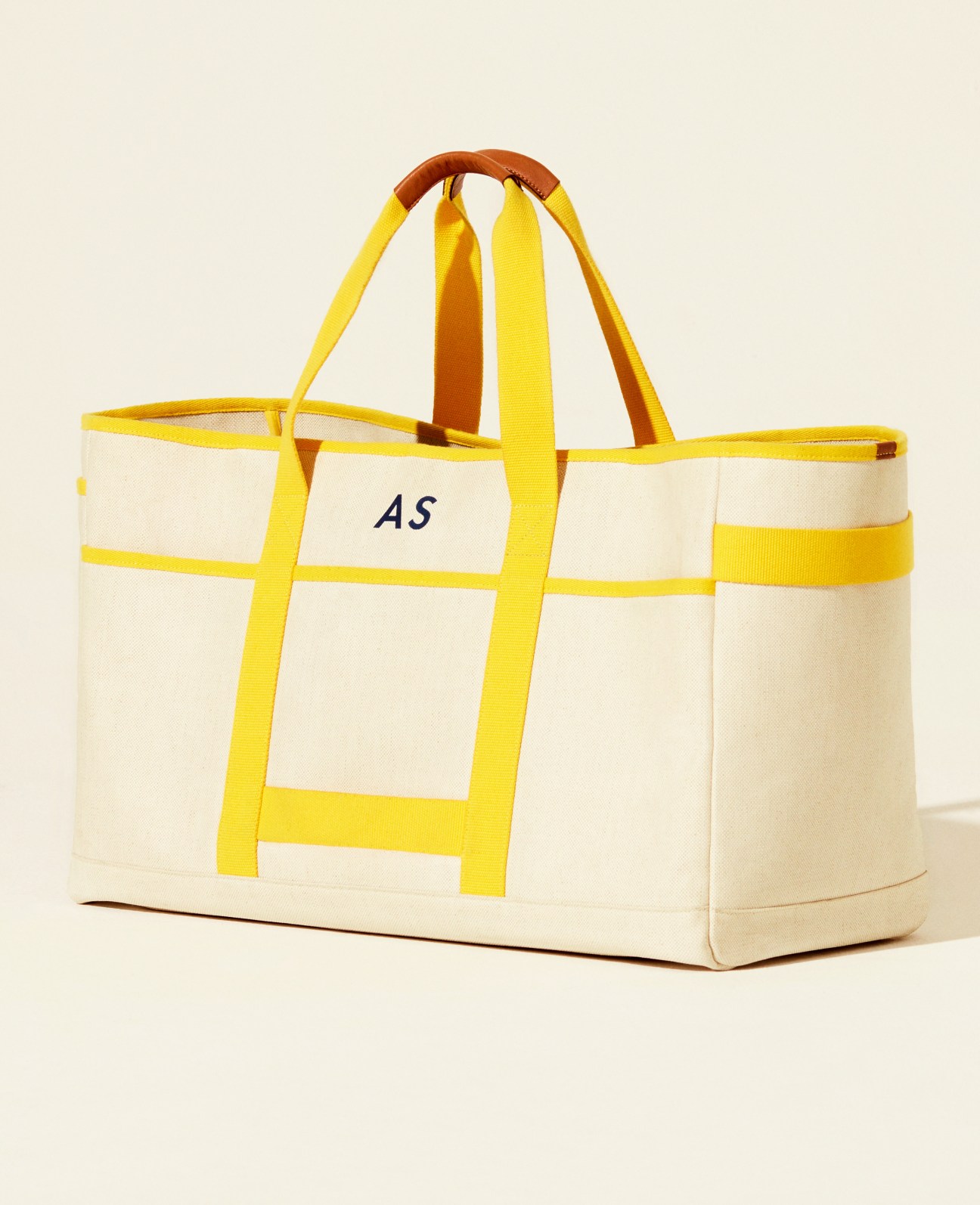 Cream canvas tote bag with yellow webbing straps and handles, featuring 'AS' monogram embroidery.