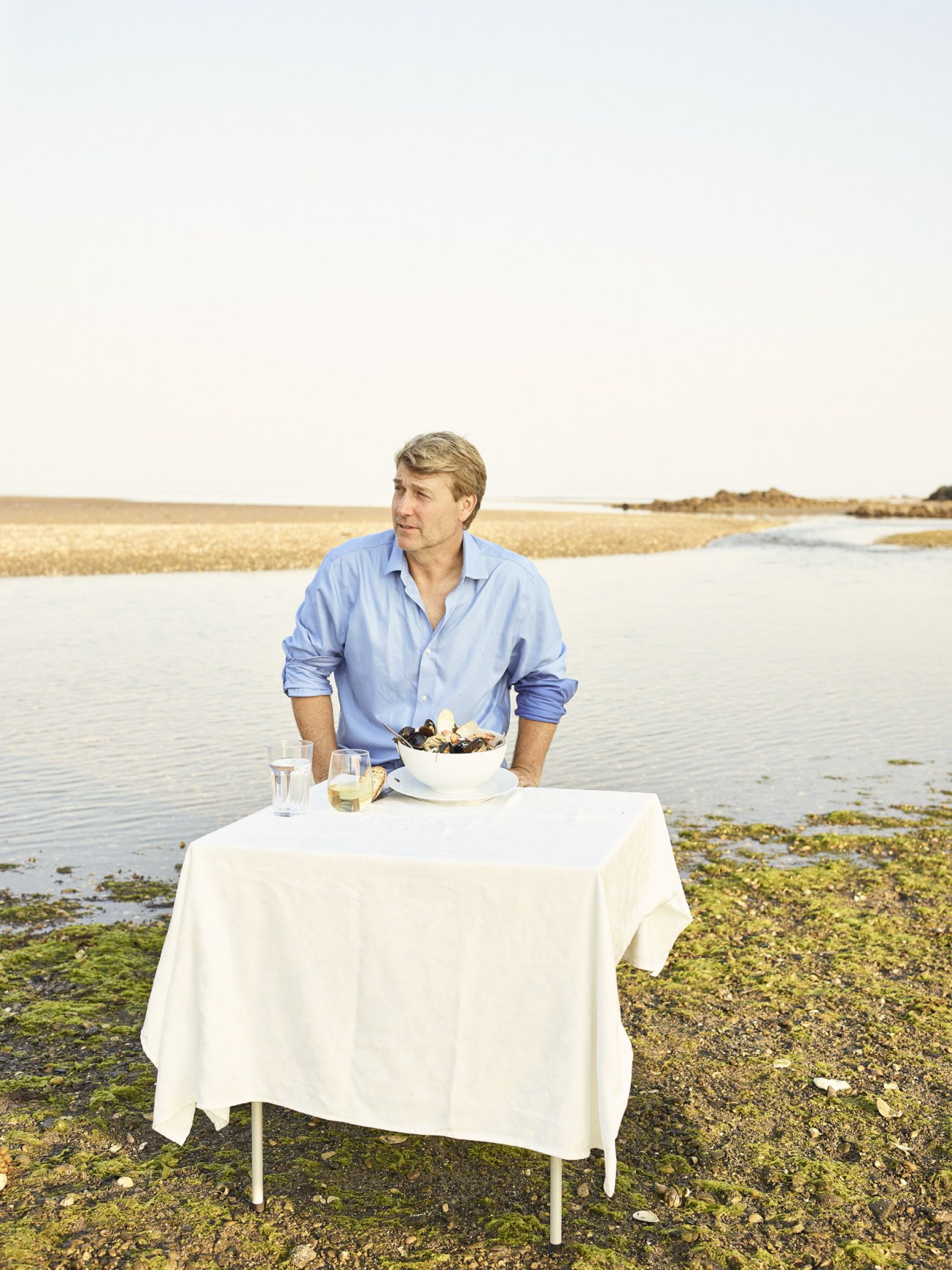 Explorer Richard Wiese dining at a white-clothed table on a tidal flat in Westport, Connecticut, with a bowl of seafood stew and wine glasses.