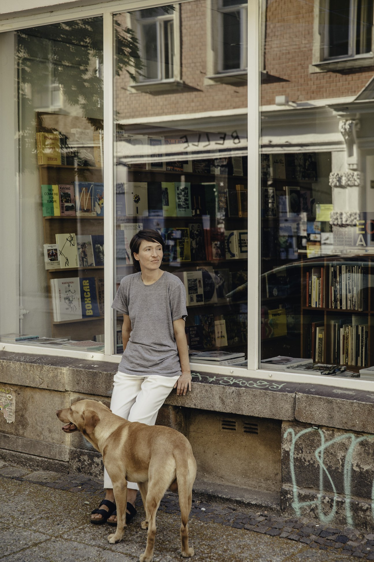 Woman standing outside a shop window with a brown dog on the street.