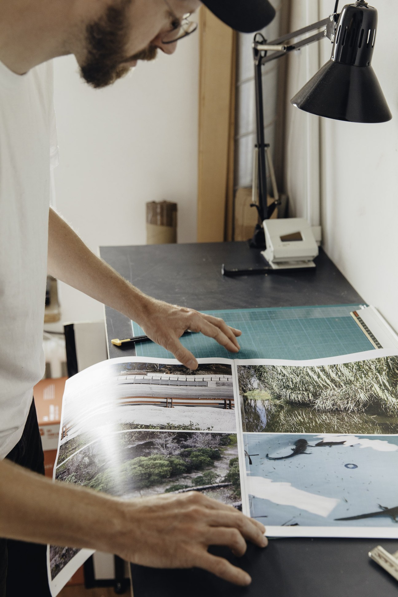Graphic designer reviewing printed publications at his desk under a black desk lamp.