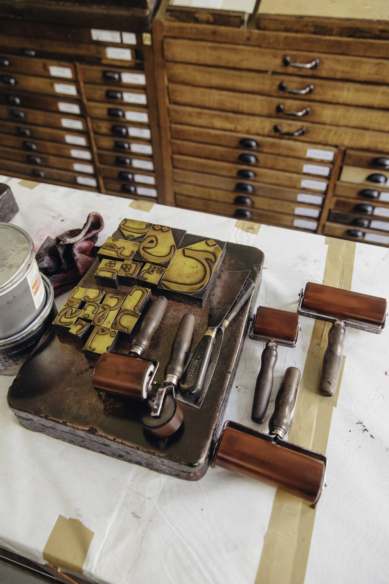 Wooden drawers with metal handles containing organized letterpress metal type blocks and printing elements.