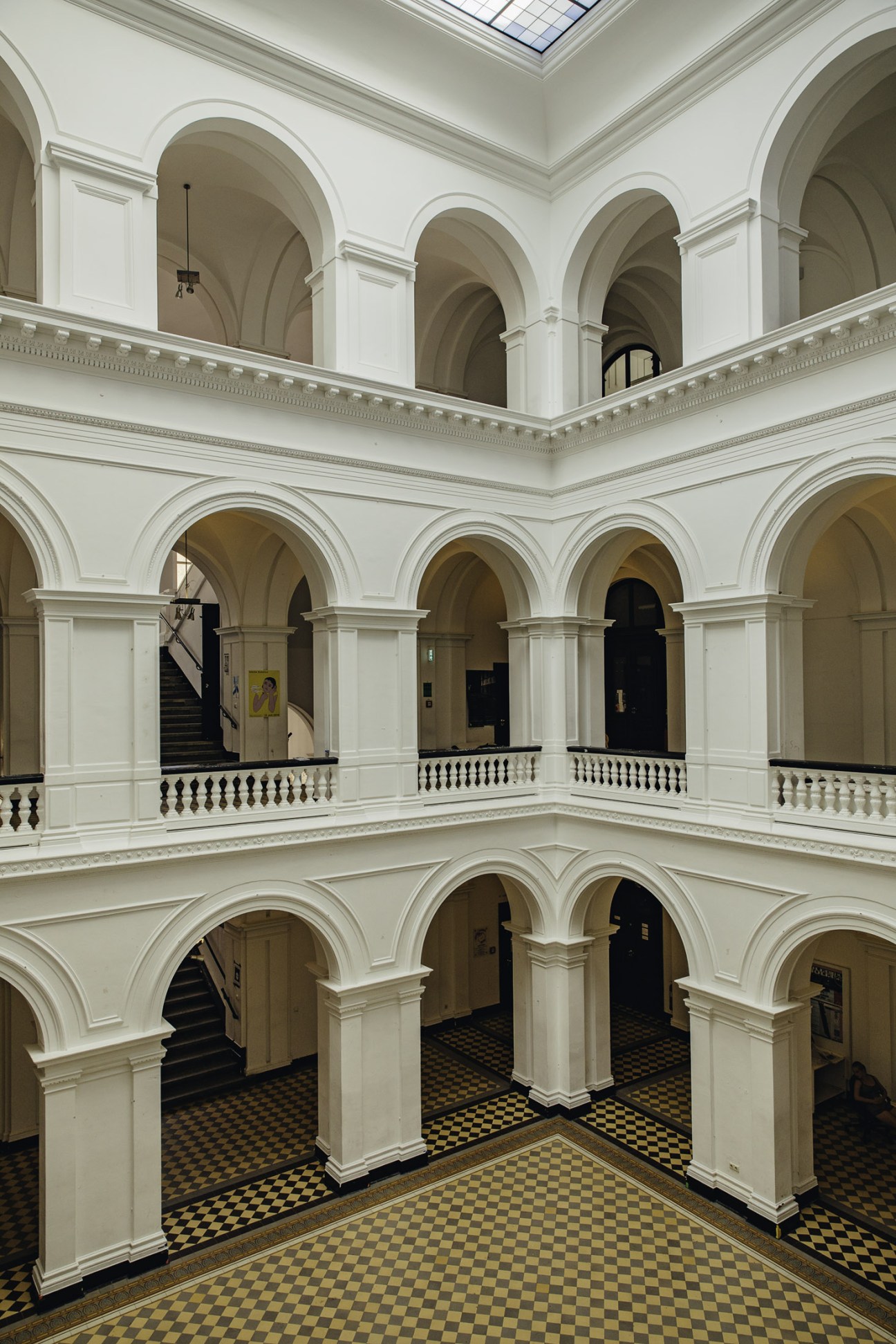 Multi-story classical atrium with white arched colonnades and ornate balustrades surrounding a light-filled central void.