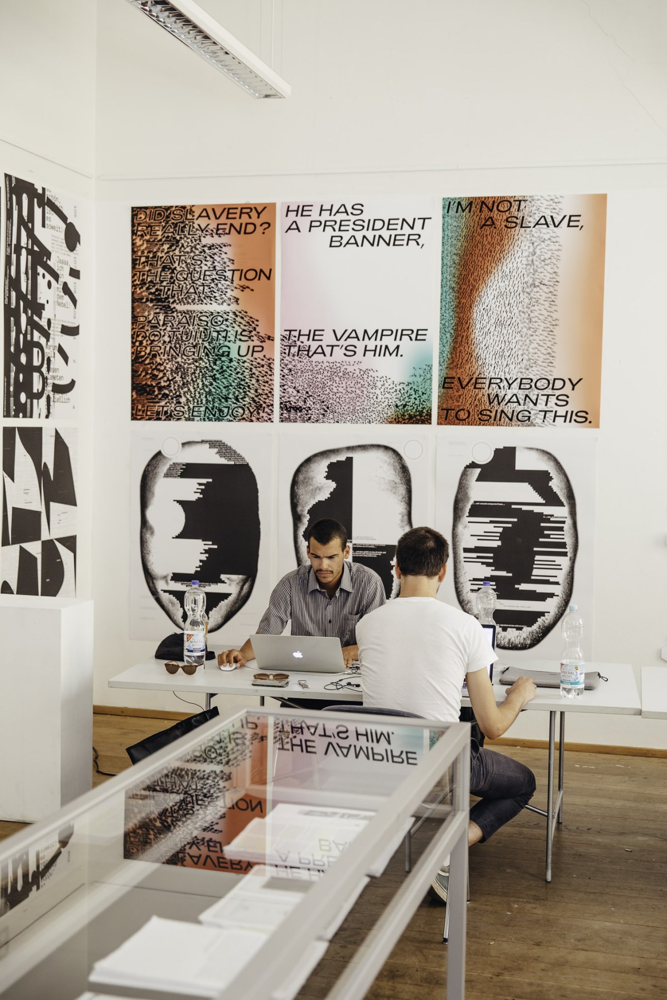 Two people collaborate at a desk in a bright studio space decorated with typographic wall art.