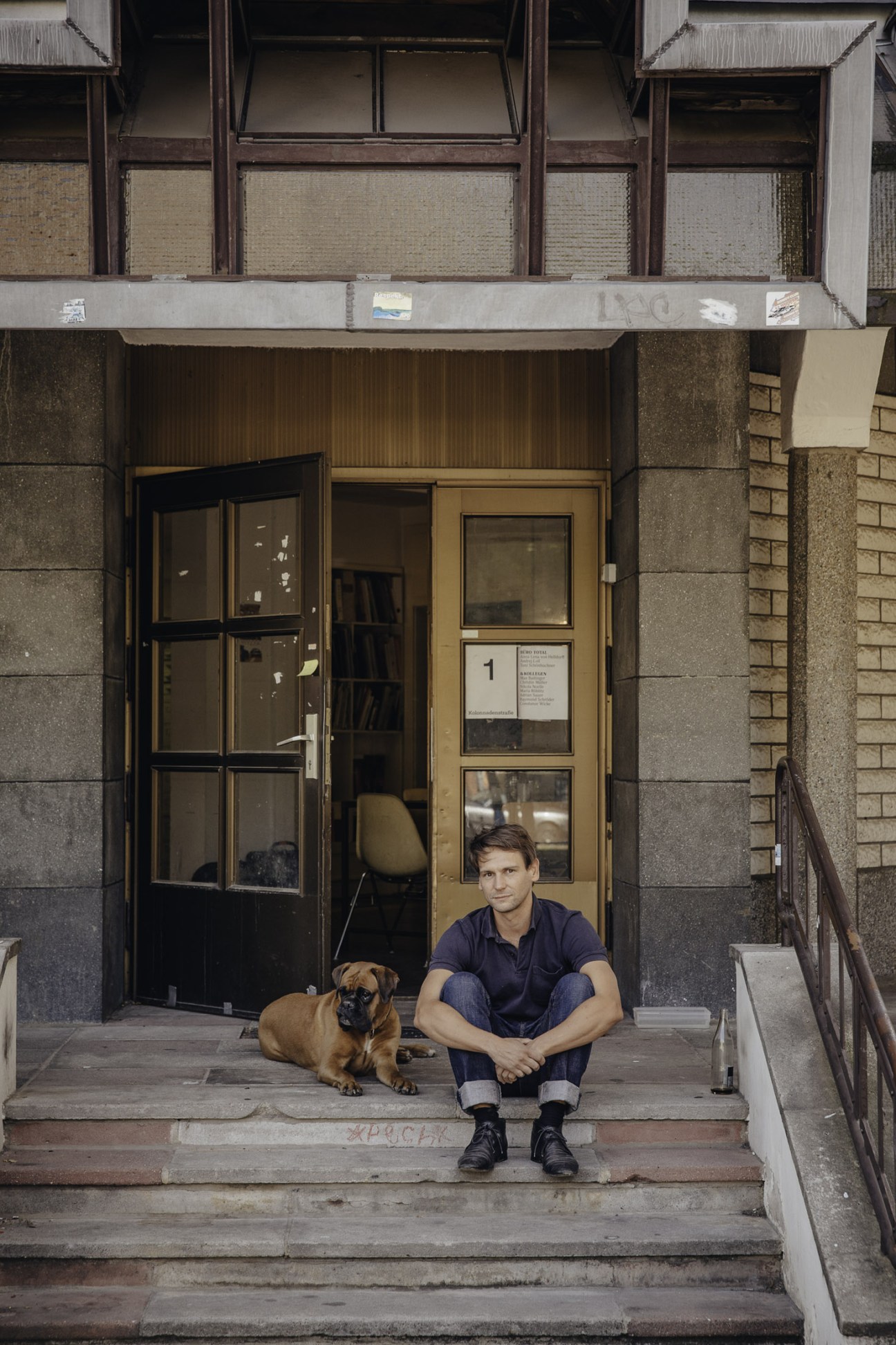 Graphic designer Toni Schönbuchner sits on studio steps with his boxer dog Ella outside Arc's office on Kolonnadenstrasse.