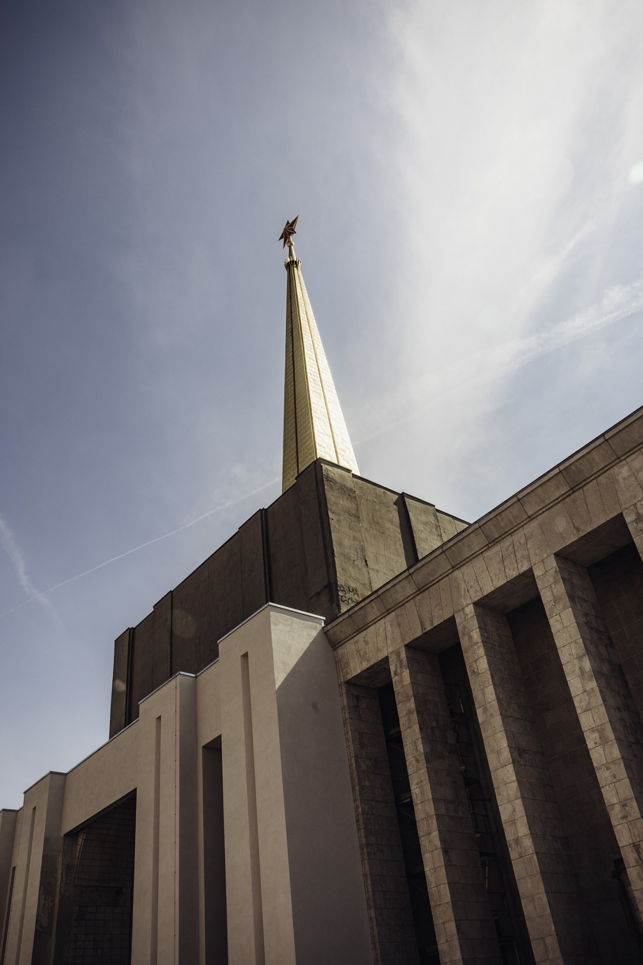 Tall spire with golden star on top rises above historic stone building against cloudy sky.