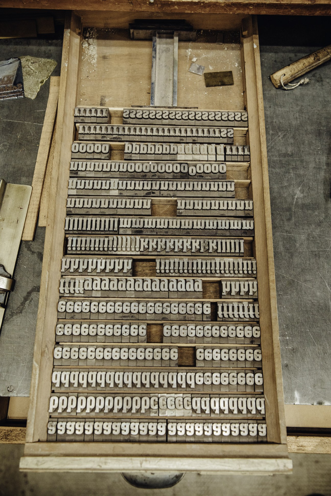 Wooden drawer containing arranged metal letterpress type blocks and characters.