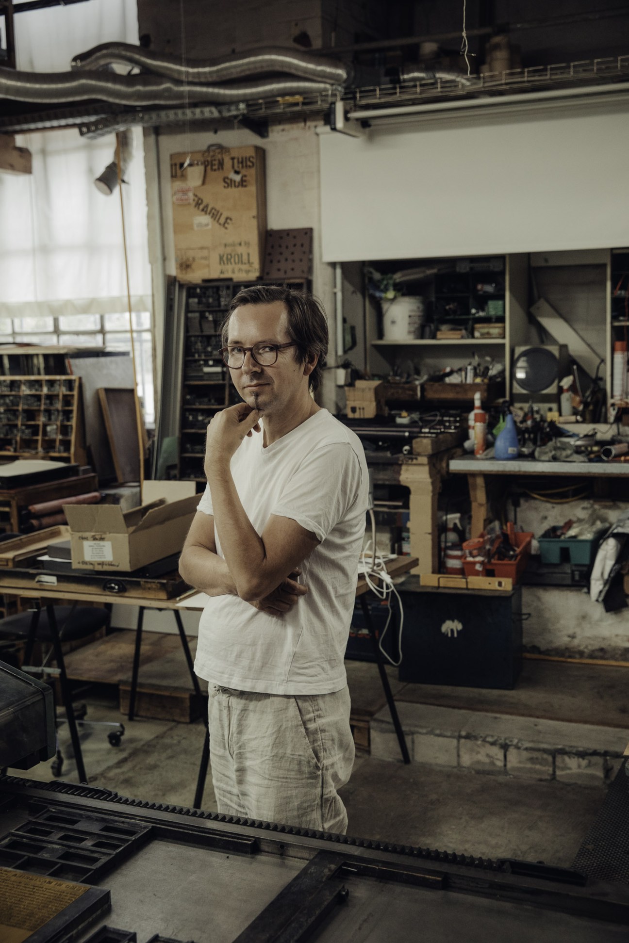 Printer Thomas Siemon stands in his workshop surrounded by letterpress equipment and materials.