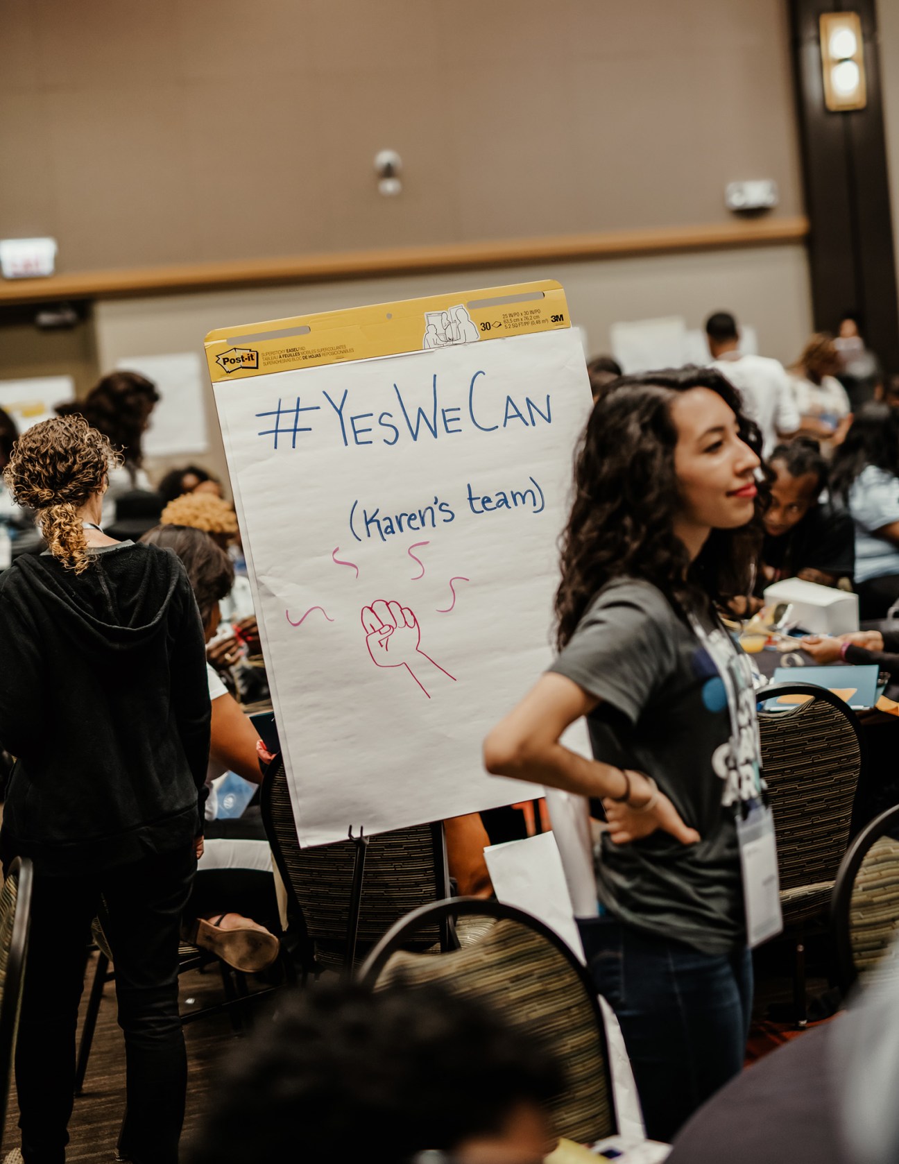 Young activists at Obama Foundation Community Leadership Corps bootcamp hold a Post-it note sign reading '#YesWeCan (Karen's team)' with a raised fist drawing.
