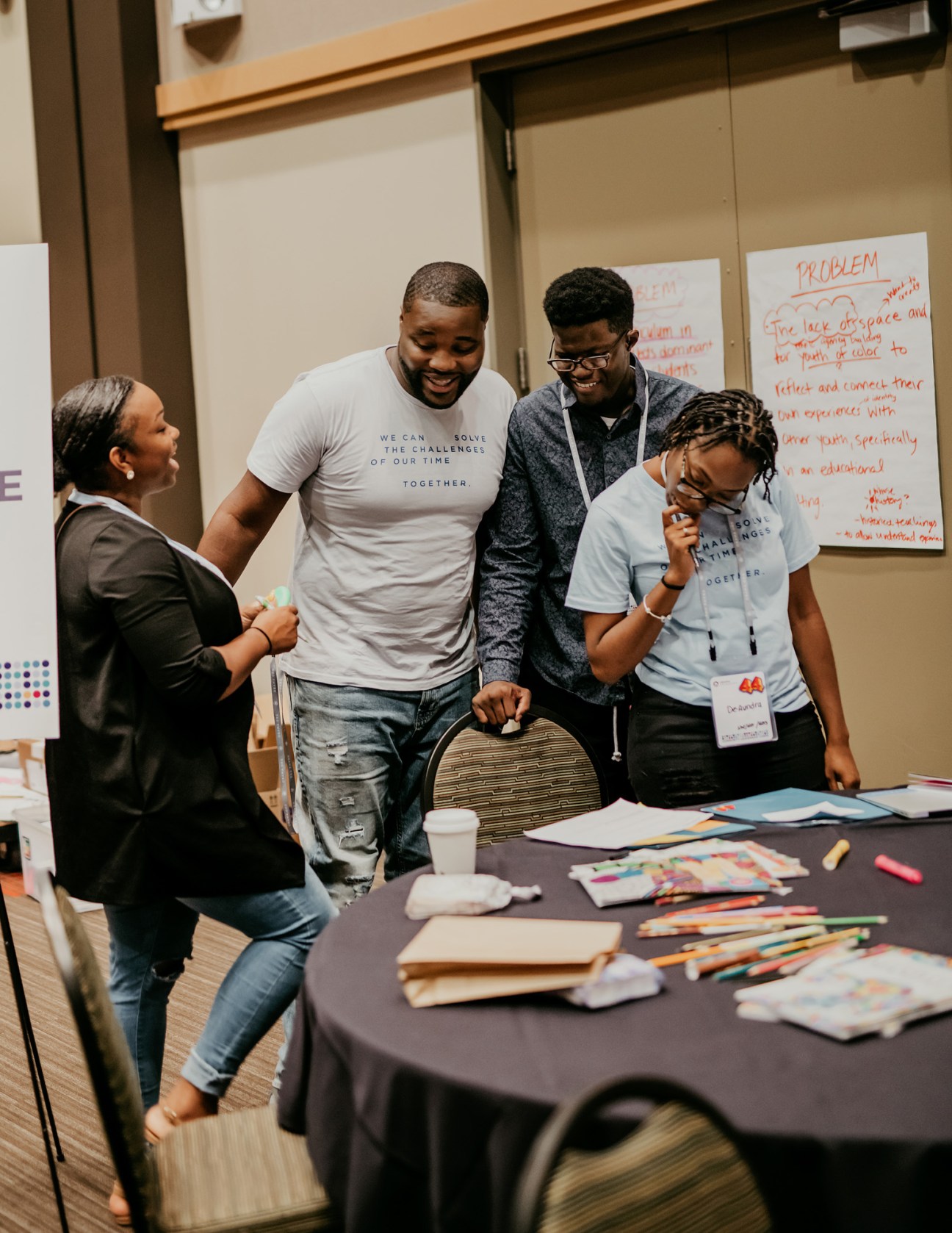 Four young people collaborate around a table covered with art supplies and papers during a Community Leadership Corps bootcamp.