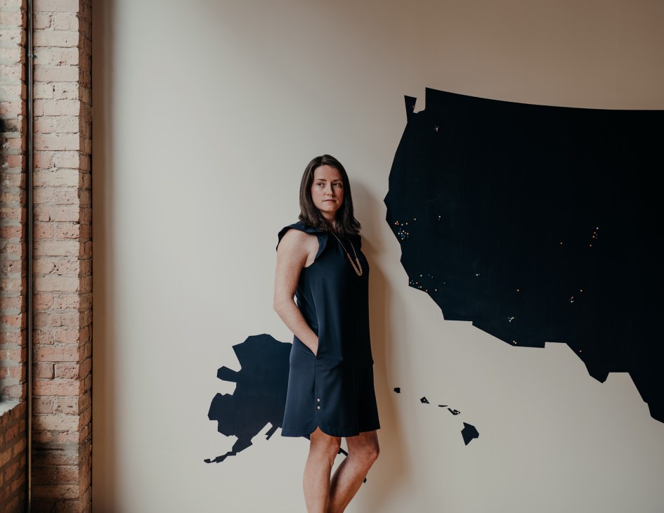 Woman in black sleeveless dress standing against wall with silhouette graphics of US map outline.