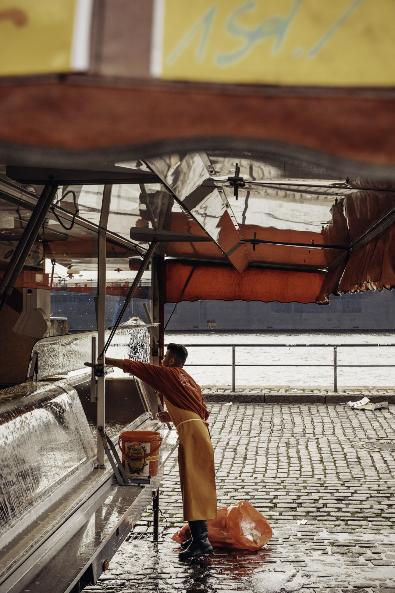 Market vendor adjusting awning at Hamburg Fish Market during morning clean-up.