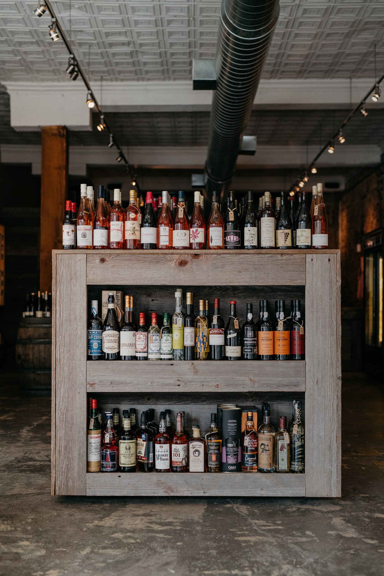 Wooden shelving display with bottles of wine arranged on three shelves in a wine bar setting.