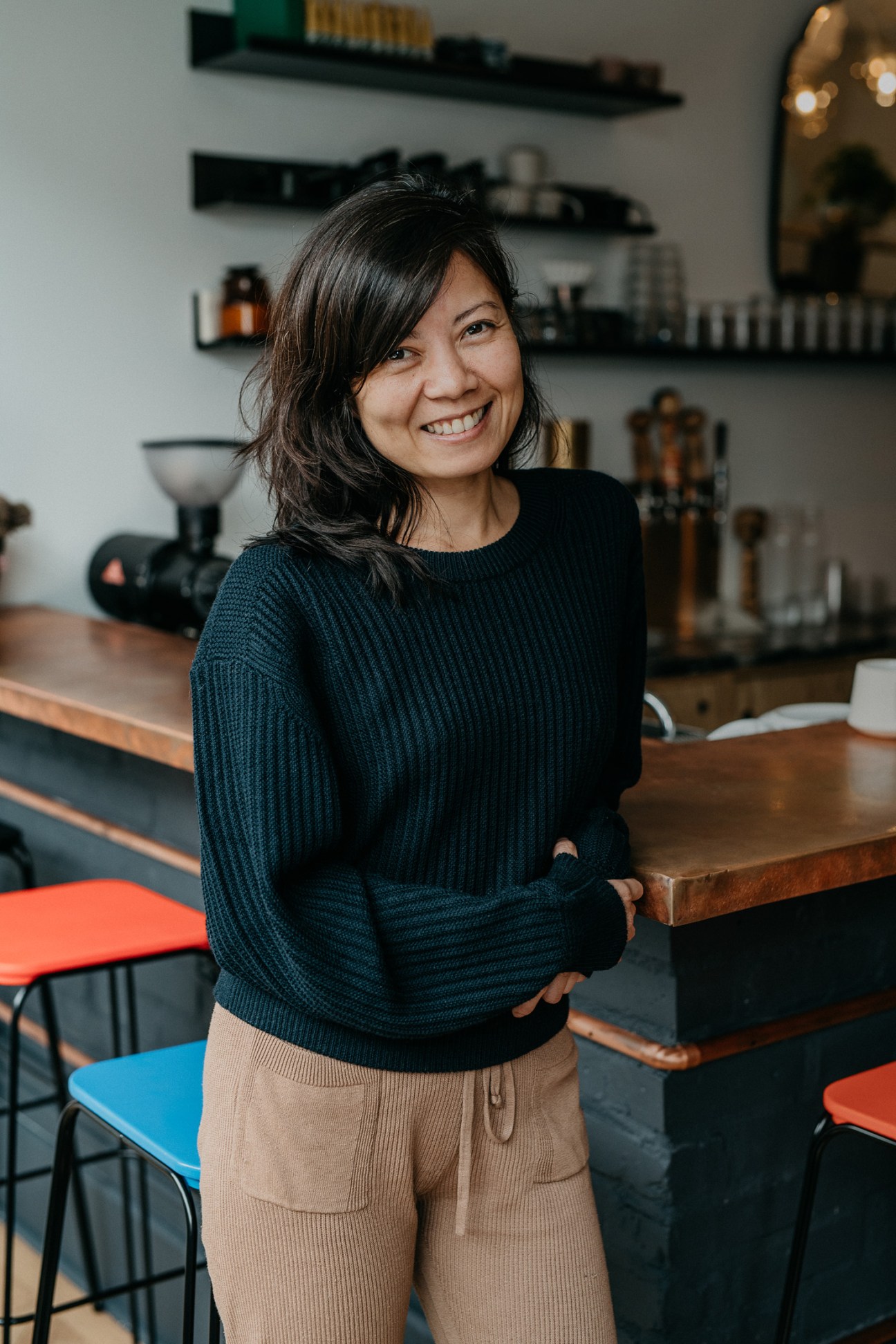 Woman smiling in a bright coffee shop with shelves of products in the background.