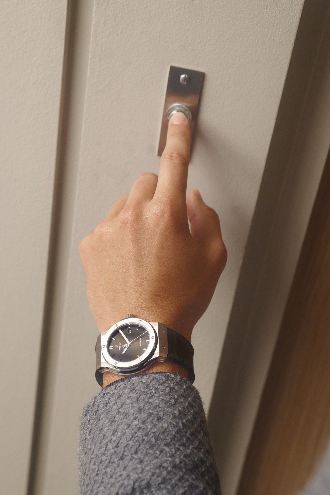 Hand wearing dark jacket and Hublot watch pressing an elevator button