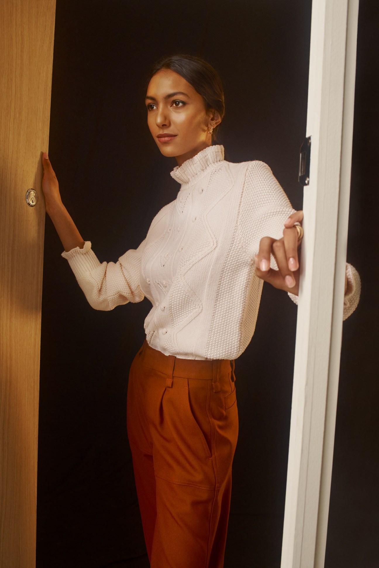 Woman in cream jumper with dark trousers, earrings and ring