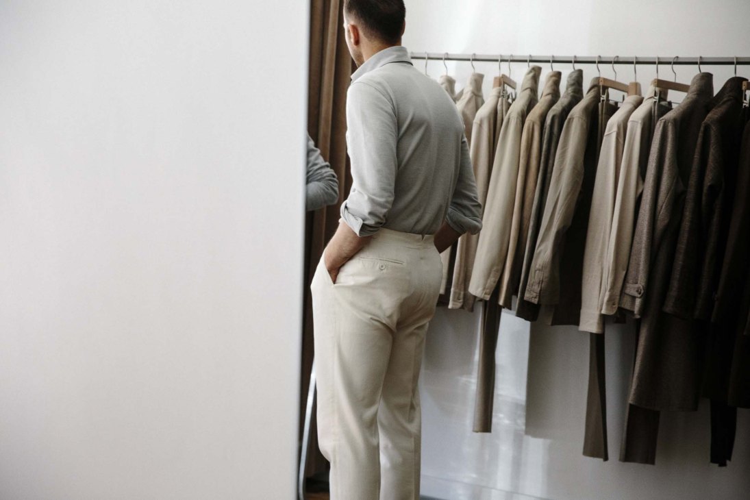 Man being fitted for tailored trousers at Stòffa trunk show with garment rack in background.