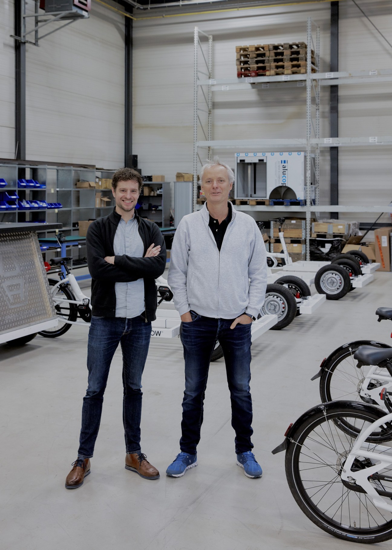 Wytze van Mansum and Jorrit Kreek stand in an Urban Arrow warehouse with cargo bikes and pallets.