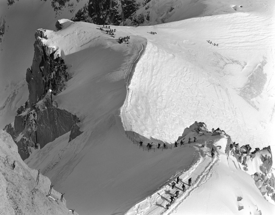 Aerial view of climbers descending snowy slopes of la Vallée Blanche with glacier and rock formations visible.