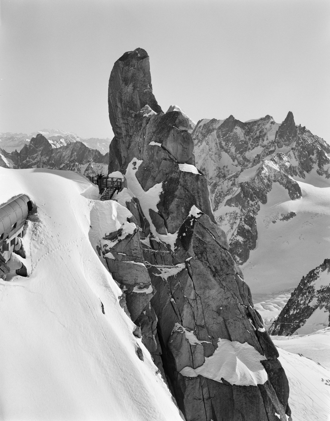 A towering granite rock formation rises from snow, with jagged peaks visible in the misty background.