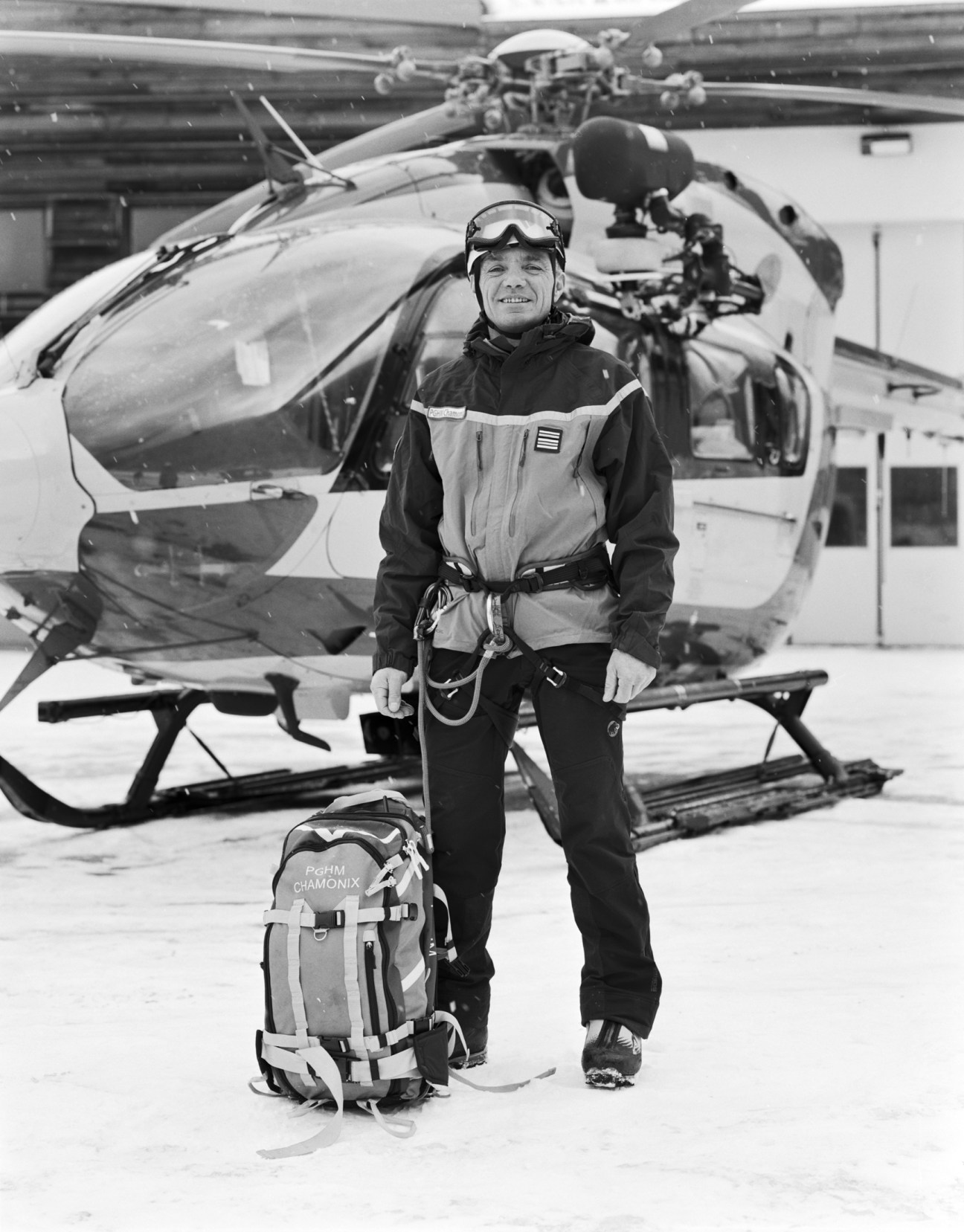 Stéphane Bozon in rescue gear stands before a helicopter with climbing equipment and harness.