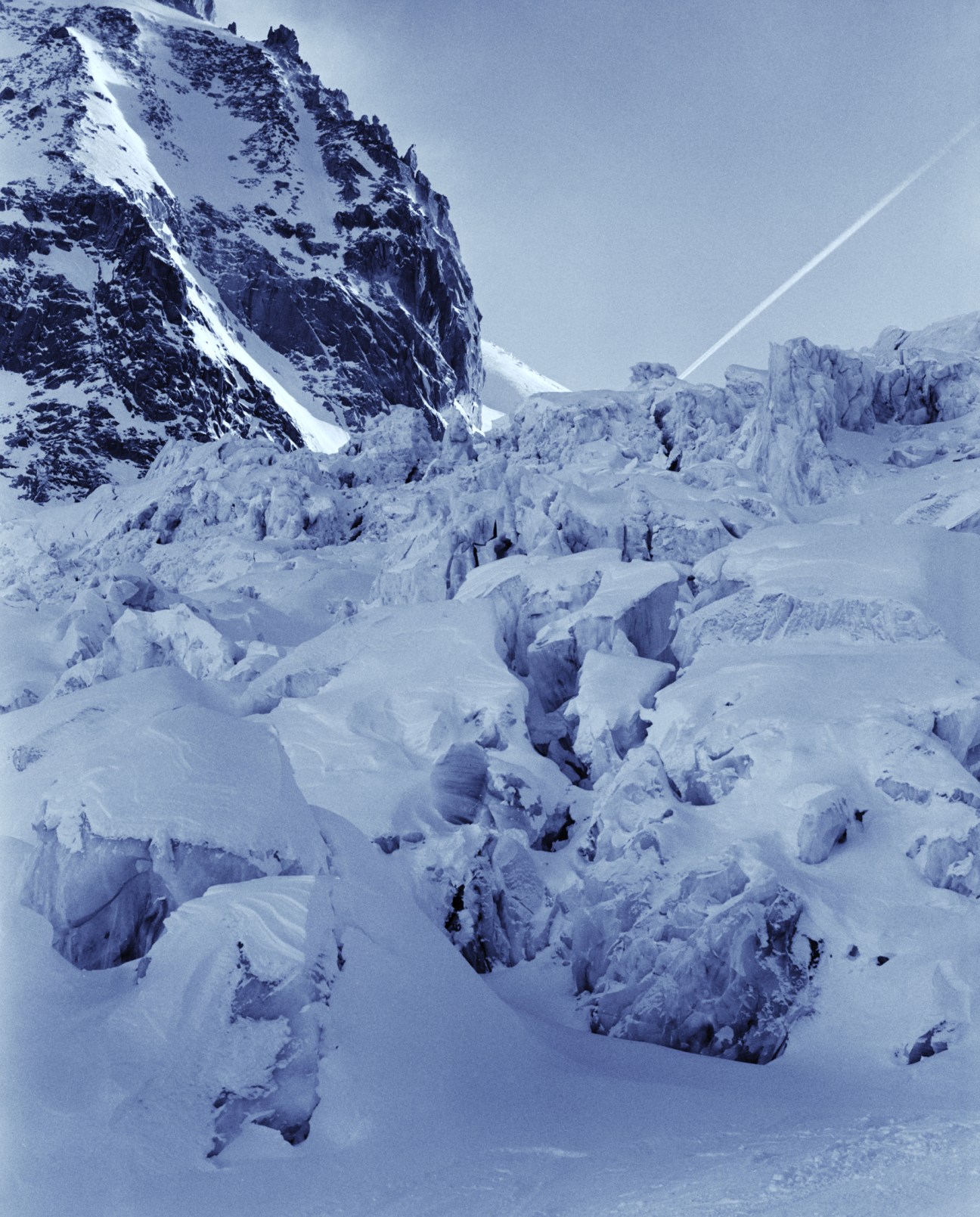 Snow-covered crevasses and ice formations on Glacier du Géant with rocky mountain peaks in the distance.