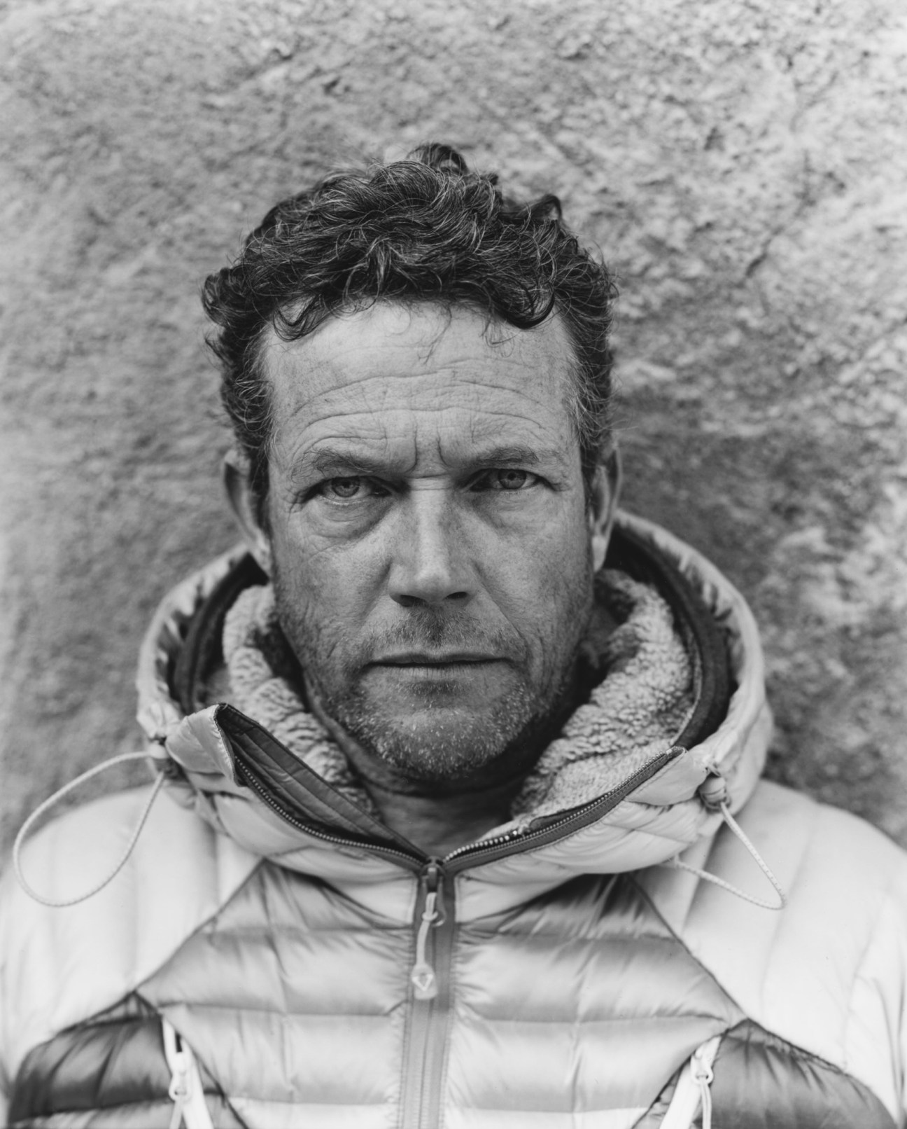 Black and white portrait of Didier Chenevoy wearing a white quilted jacket against a textured wall.