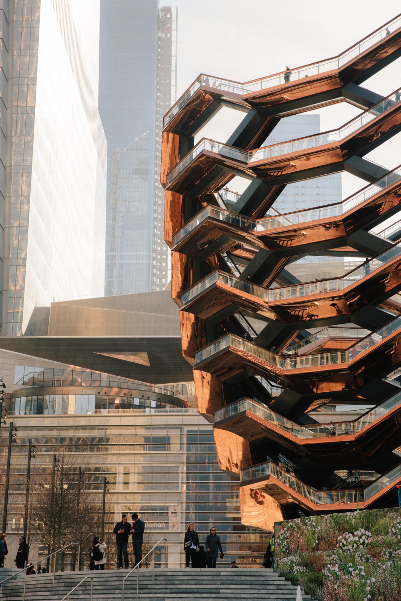 The Vessel structure at Hudson Yards with copper-colored staircase architecture and surrounding skyscrapers.