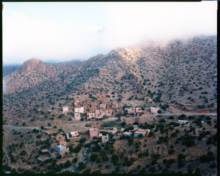 A misty morning aerial view of a Moroccan village nestled in a valley surrounded by arid hills and mountains.