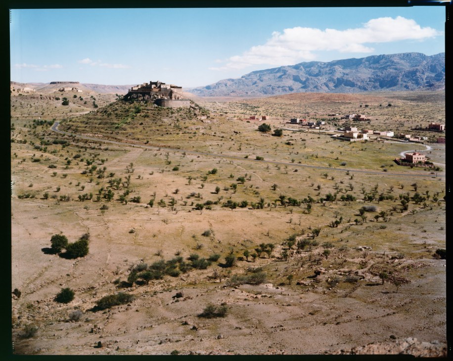 Kasbah Tizourgane fortified structure perched on rocky hilltop overlooking vast arid plain with scattered settlements below.