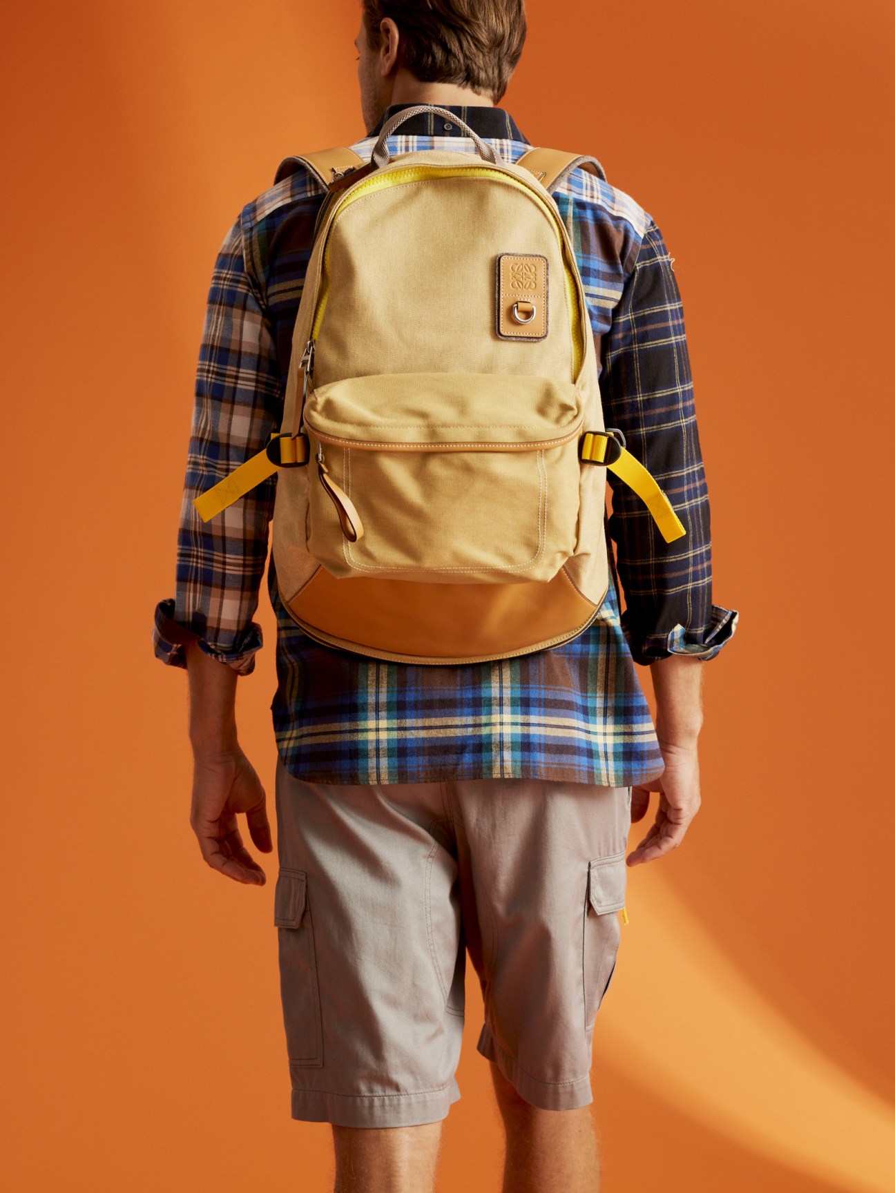 Man wearing Eye Loewe Nature canvas backpack in cream and tan with yellow straps over a plaid shirt.