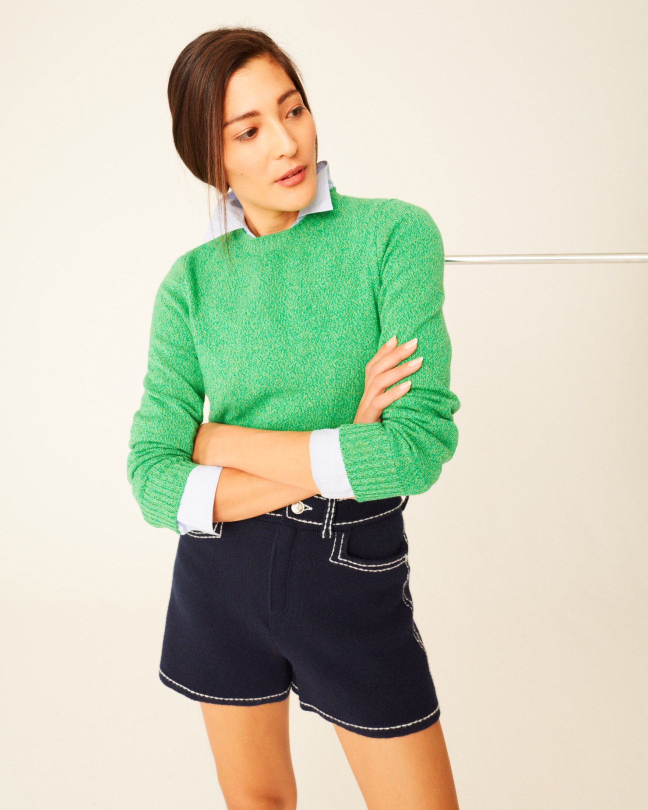Woman wearing a green knit jumper, white collared shirt, and navy shorts with white stitching detail.