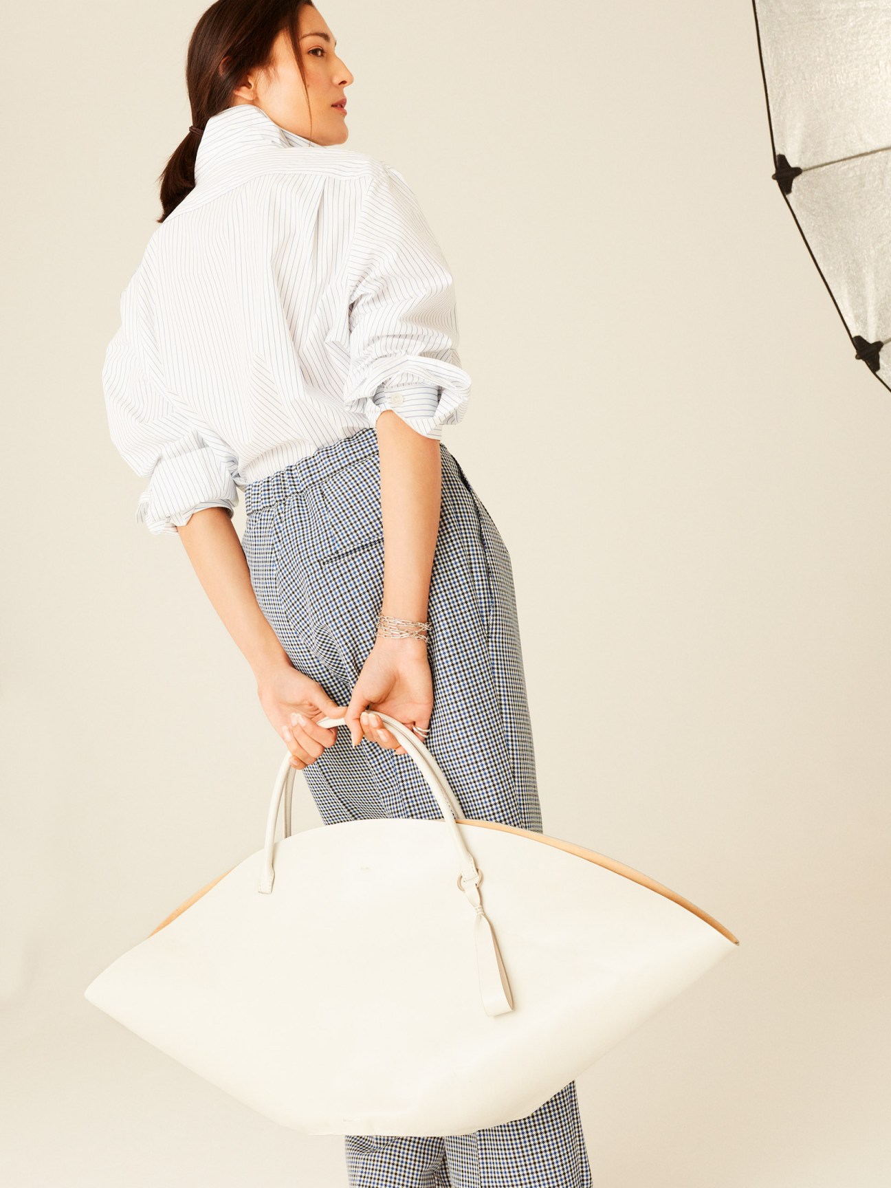 Woman wearing white shirt, checked trousers, and carrying white clutch from Bottega Veneta.