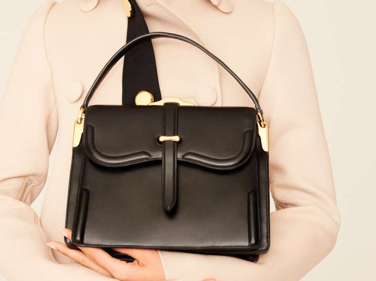 Woman wearing a beige coat and holding a black leather Prada bag with gold hardware