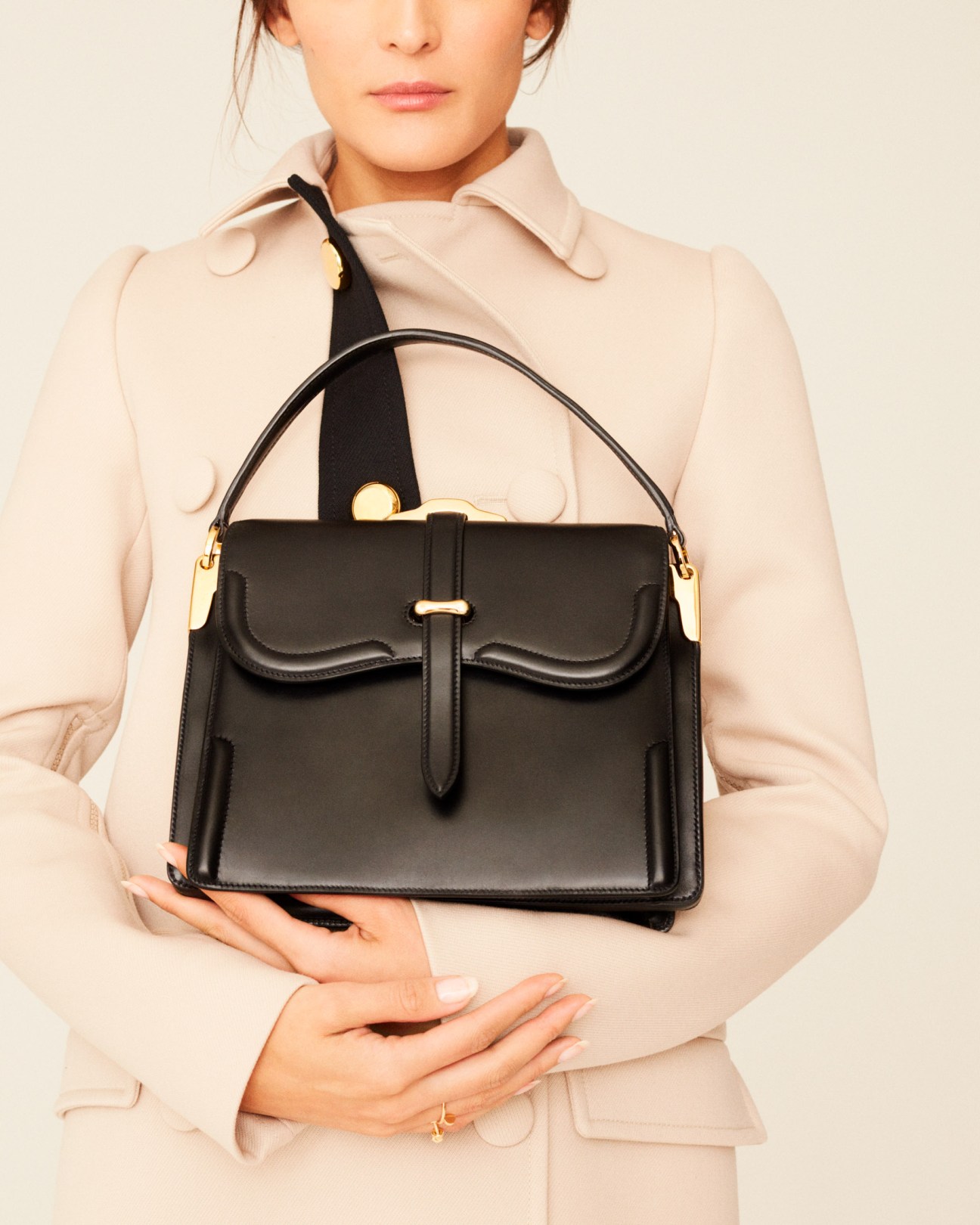 Woman wearing a beige coat and holding a black leather Prada bag with gold hardware