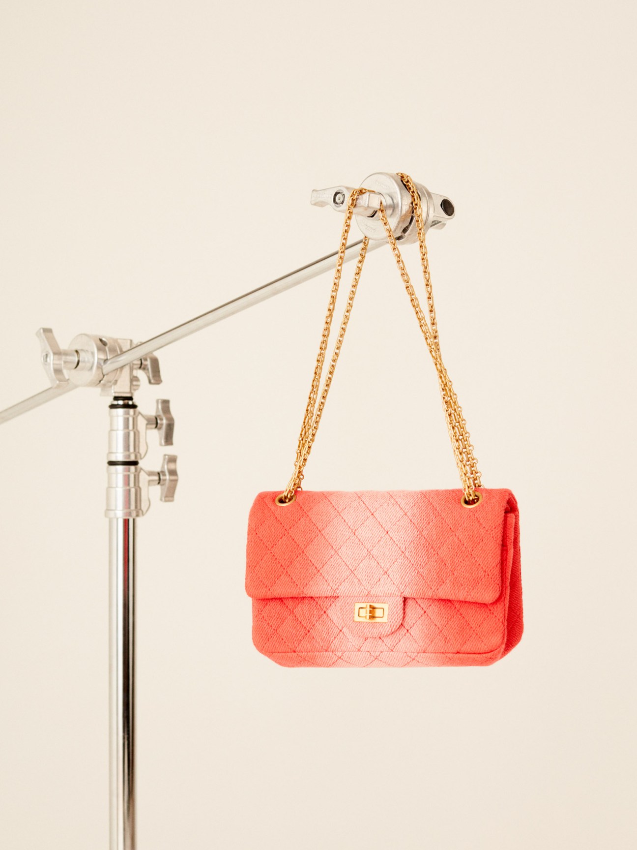 Coral quilted shoulder bag with gold chain strap hanging from a studio light rig against a beige background.