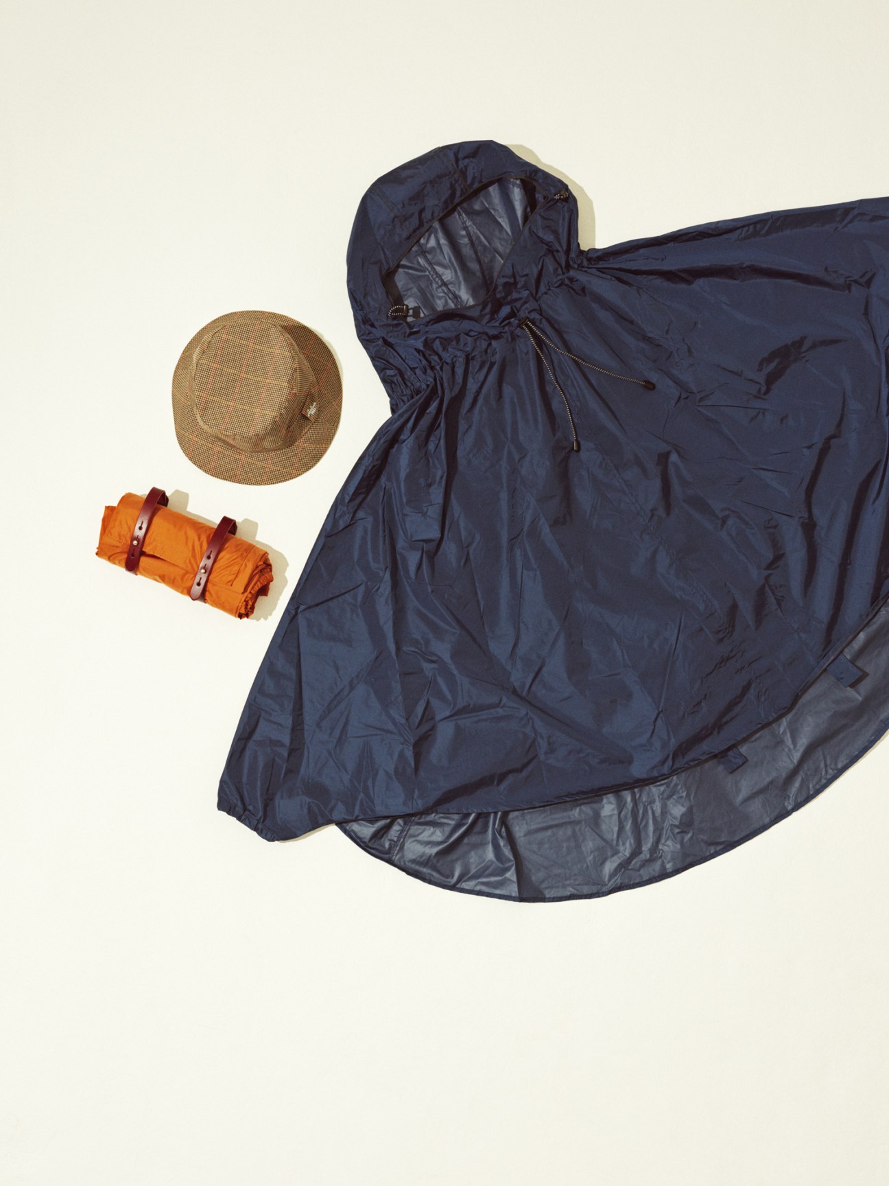 Rain capes by Brooks England in navy blue with a tan hat by Sealup and orange rolled fabric on cream background.