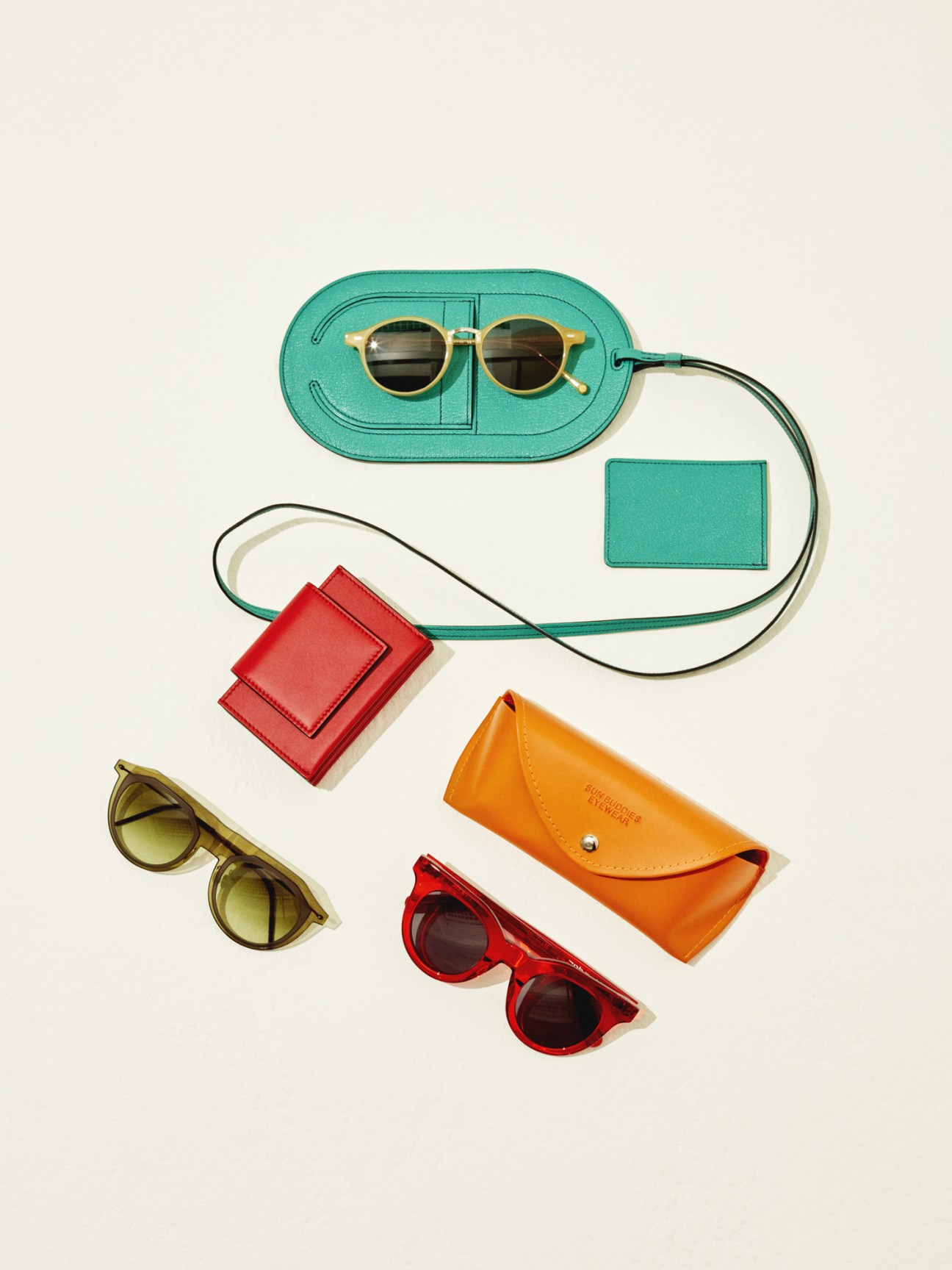 Colorful sunglasses and accessories arranged on a neutral background including turquoise and red frames with matching cases and pouches.