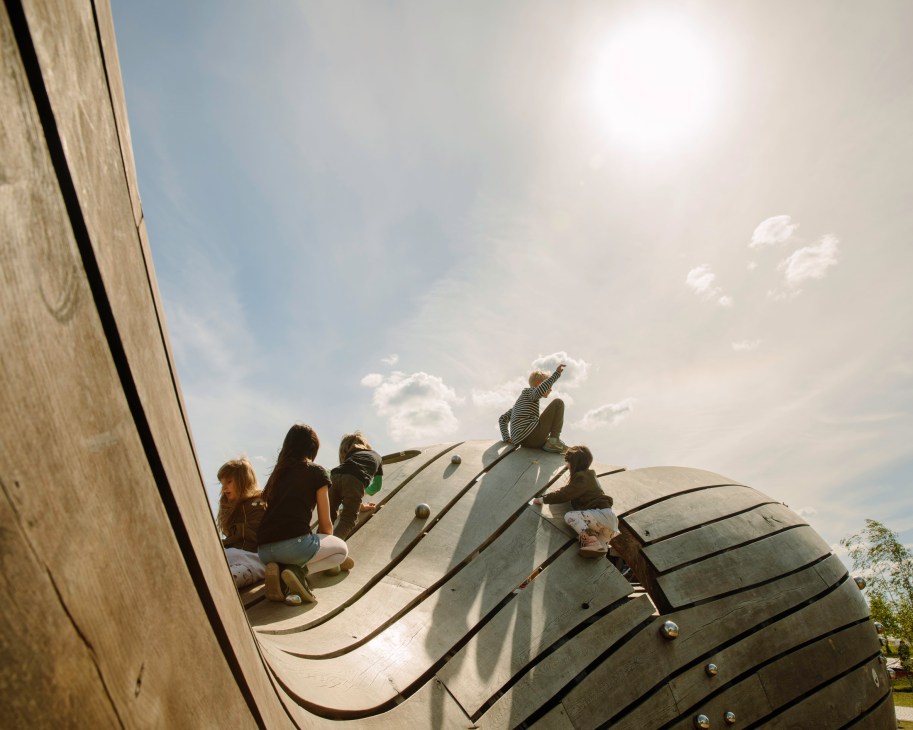 Children playing on a large wooden blue whale climbing structure at Gärten der Welt park in Berlin.